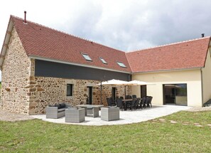 A stone house with a tiled roof, outdoor seating area, and a covered patio. - Spacious family house with sauna and garden (Rives-d'Andaine)