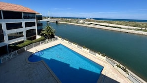 A pool with a clear view of the sea and a building with balconies.