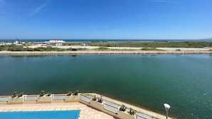 A coastal view with a clear sky, a calm body of water, and a distant shoreline with buildings and vehicles.
