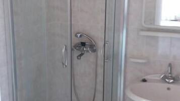A glass-enclosed shower with a handheld showerhead, a white sink, and a mirror above the sink.