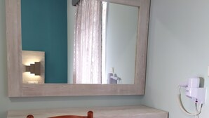 A bathroom with a wooden chair, a large mirror, and a hairdryer on the wall. - Giannis Studios Alykes (Zakynthos)