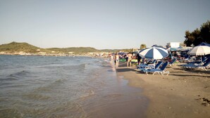 A beach with clear water, umbrellas, and lounge chairs. - Giannis Studios Alykes (Zakynthos)