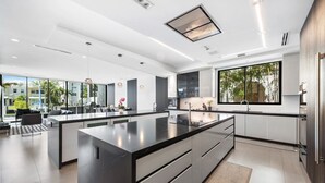 A modern kitchen with a large central island, sleek cabinetry, and a large window providing a view of the outdoors. - Boardwalk Mansion Lauderdale Villa: Private Pool, Hot Tub, Mini-Golf & Guest House (Fort Lauderdale)