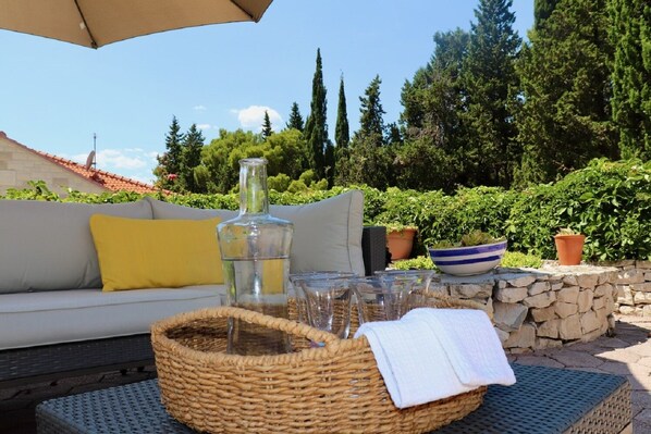An outdoor seating area with a wicker basket, a glass bottle, and a bowl on a table.
