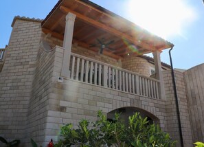 A building with a brick facade, a wooden balcony with a white railing, and a ceiling fan.