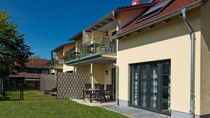 A modern two-story building with a balcony, outdoor seating, and a fenced garden area. - Apt. STURMMÖWE ​​- Fantastic new apartment close to the beach in Gollwitz! (Insel Poel / OT Gollwitz)