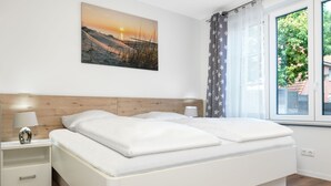 A modern bedroom with a large bed, a nightstand, a lamp, and a window with curtains. - Apt. STURMMÖWE ​​- Fantastic new apartment close to the beach in Gollwitz! (Insel Poel / OT Gollwitz)
