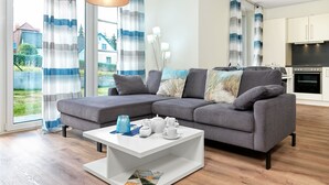 A modern living room with a grey sectional sofa, a white coffee table, and a kitchen in the background. - Apt. STURMMÖWE ​​- Fantastic new apartment close to the beach in Gollwitz! (Insel Poel / OT Gollwitz)