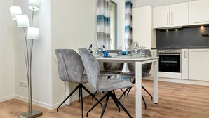 A modern kitchen with a dining area, featuring a white table, grey chairs, and a floor lamp. - Apt. STURMMÖWE ​​- Fantastic new apartment close to the beach in Gollwitz! (Insel Poel / OT Gollwitz)