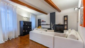 A living room with a white sofa, wooden beams, a TV, and a bookshelf. - GuestHost - Central Ferrara Apartment! x7 (Ferrara)