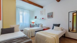 A room with two beds, a window with curtains, a small table with a lamp, and wall art. - GuestHost - Central Ferrara Apartment! x7 (Ferrara)