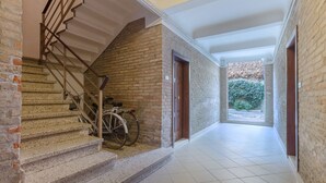 A hallway with a staircase, a bicycle, and a view of greenery outside. - GuestHost - Central Ferrara Apartment! x7 (Ferrara)