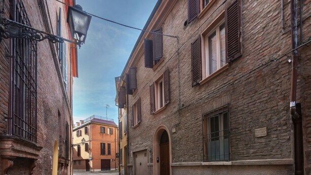 A narrow cobblestone street flanked by historic buildings with arched doorways and shuttered windows. - GuestHost - Central Ferrara Apartment! x7 (Ferrara)