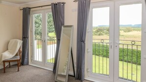 Een kamer met een grote schuifpui die uitkomt op een balkon met een metalen hek. Er staat een stoel tegen de muur en een spiegel tegen de deur aan.