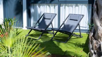 Two lounge chairs on artificial grass in front of a building with large windows and a door.