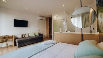 Una habitación de hotel moderna con cama, sofá, escritorio, silla, televisor, ducha y espejo.