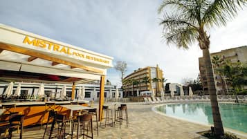 Zona de piscina amb un restaurant anomenat "MISTRAL POOL RESTAURANT", seients a l'aire lliure i una piscina.