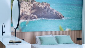 A bedroom with a bed, a bedside table, a mirror, and a wall mural of a coastal scene. - Alannia Salou Resort  (Salou)