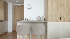 A modern kitchen with wooden cabinets, a white countertop, two bar stools, and a hanging light fixture.