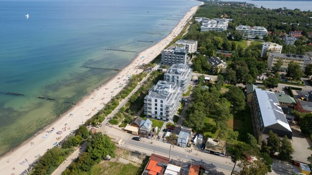 An aerial view of a coastal area with a beach, buildings, and a road.