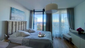 A bedroom with a bed, bedside table, lamp, and a view of the city through large windows.