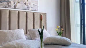 A neatly made bed with a headboard, a glass vase with a single tulip, and a tray with two white cups and saucers.
