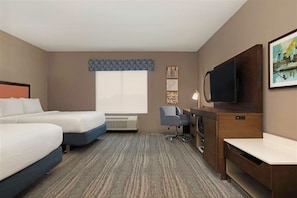 Ein Hotelzimmer mit zwei Betten, einem Schreibtisch, einem Stuhl, einem Fernseher und Bildern an den Wänden.
