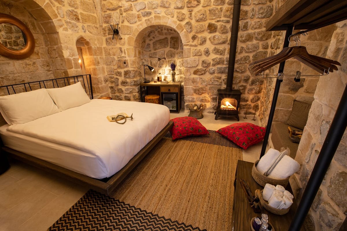 A stone-walled bedroom with a bed, a fireplace, and a wooden bench with towels.