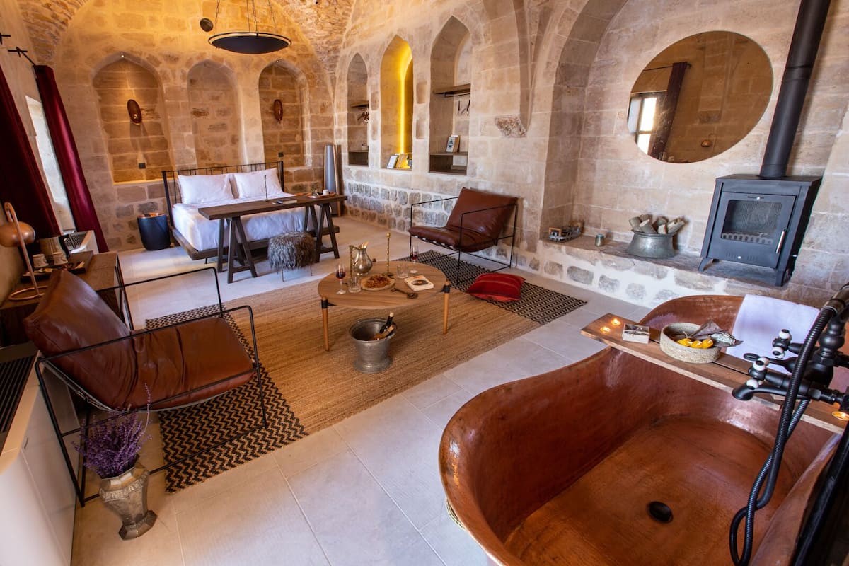 A stone-walled room with a large bathtub, a fireplace, and a dining area with a table and chairs.
