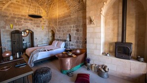 Una habitación rústica de piedra con cama, un lavabo de cobre, chimenea y un cofre de madera.