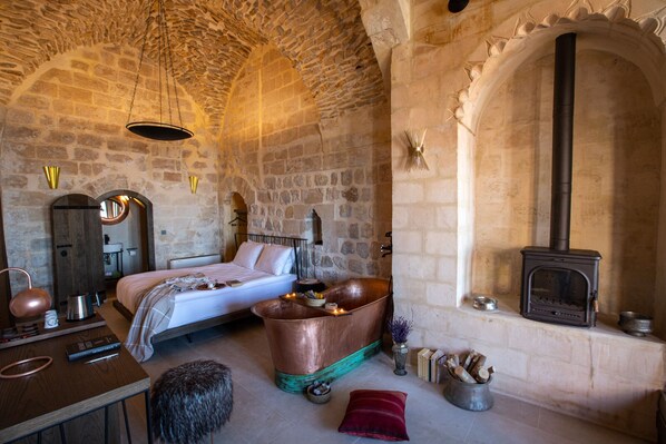 A rustic stone room with a bed, a copper basin, a fireplace, and a wooden chest. - Mirsoum Hotel (Mardin)