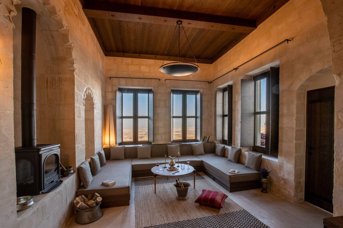 A cozy room with a stone fireplace, a wooden ceiling, and large windows offering a view of the desert.