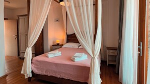 Una cama con dosel, cortinas blancas, colcha rosa y toallas ordenadas a un lado.