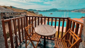 Una terraza de madera con mesa y sillas que da a un mar turquesa y montañas distantes.