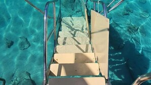 Vista despejada de la cubierta de un barco, con barandilla metálica y escalones que bajan al agua.