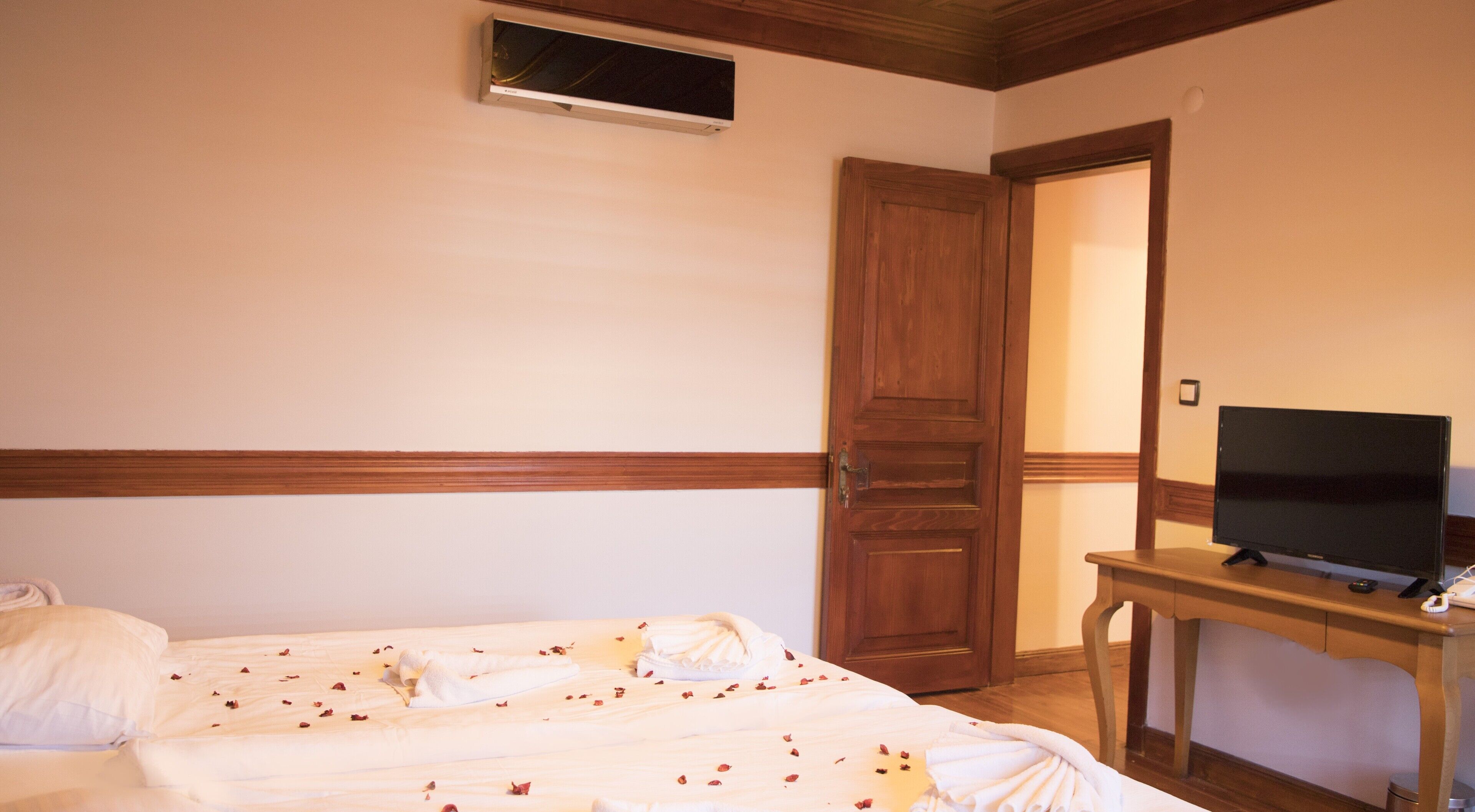 Una habitación de hotel con cama, un televisor sobre una mesa de madera y una puerta que da a otra habitación.
