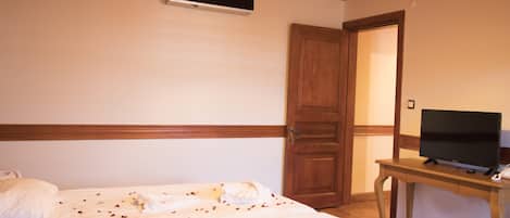 Una habitación de hotel con cama, un televisor sobre una mesa de madera y una puerta que da a otra habitación.