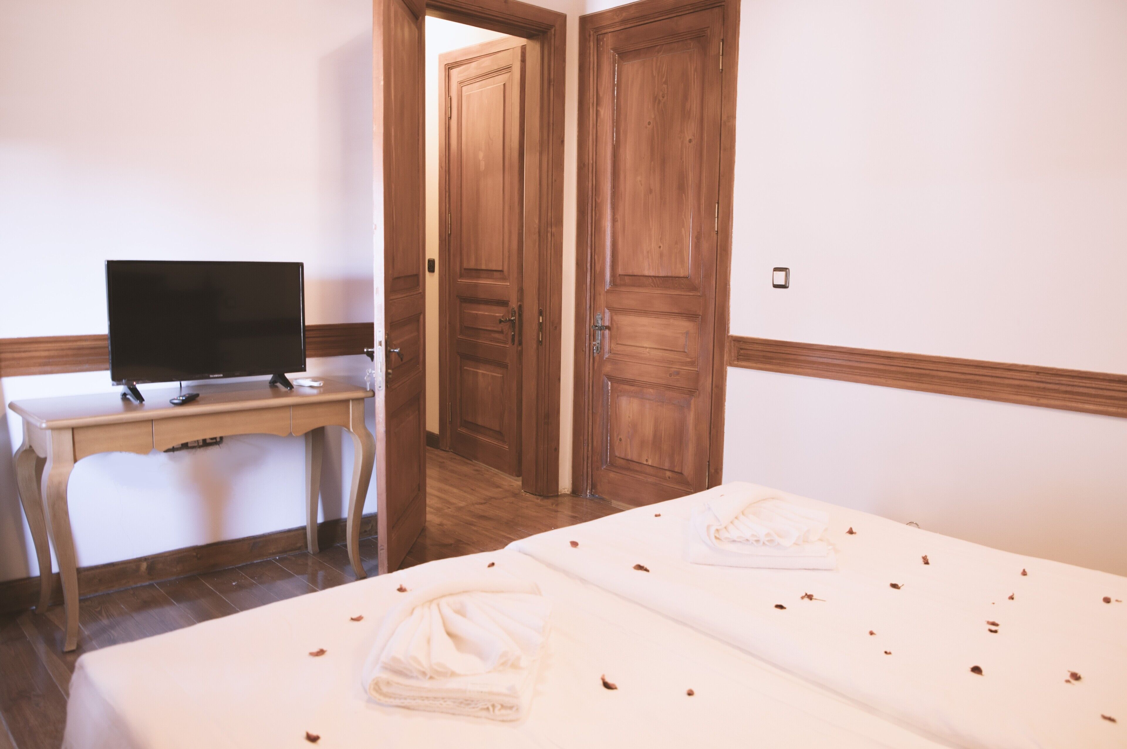 A hotel room with a bed, a desk with a television, and wooden doors.