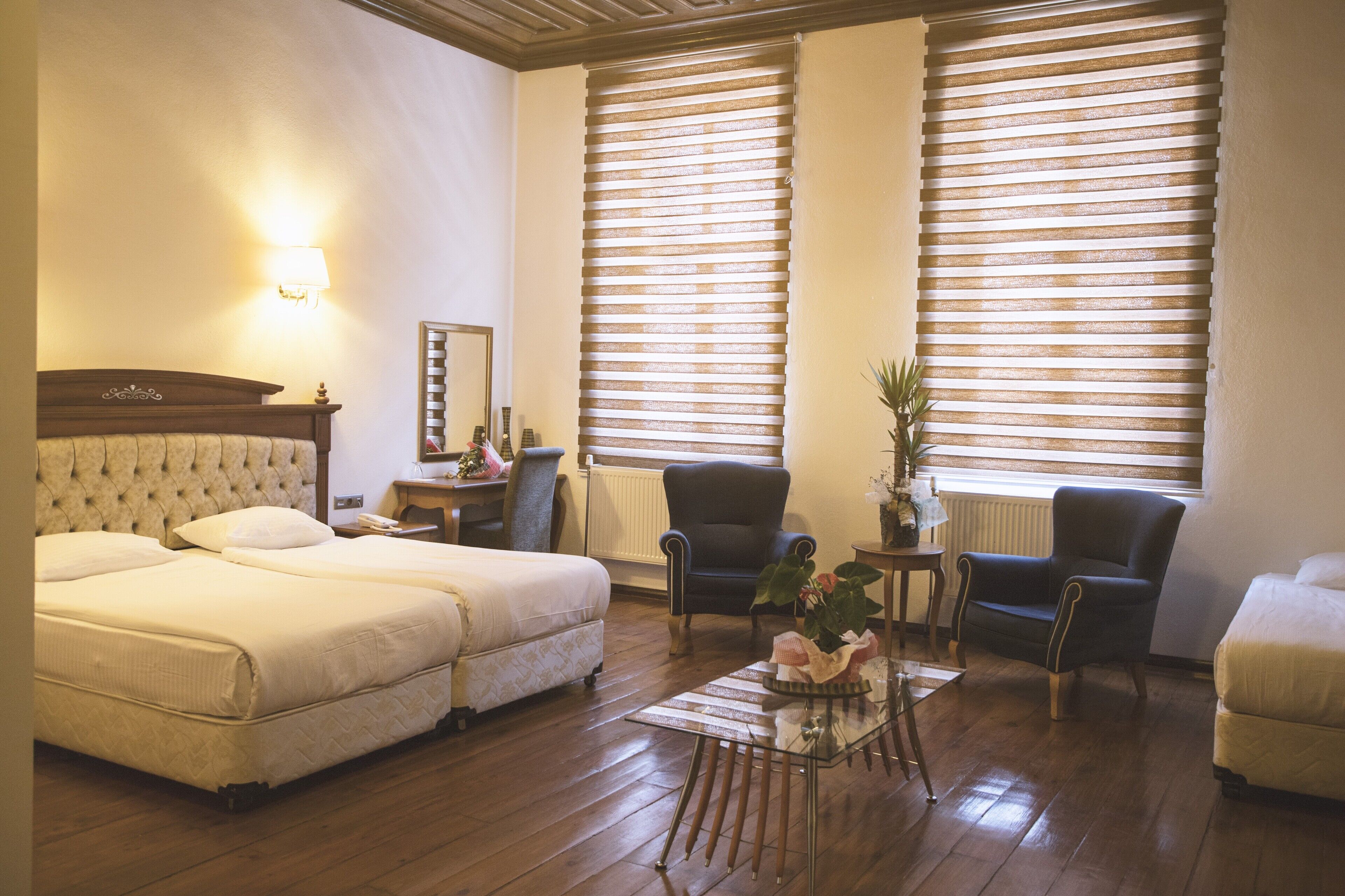 A hotel room with two beds, a small table, a chair, and a radiator.
