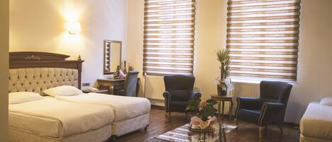 A hotel room with two beds, a small table, a chair, and a radiator.