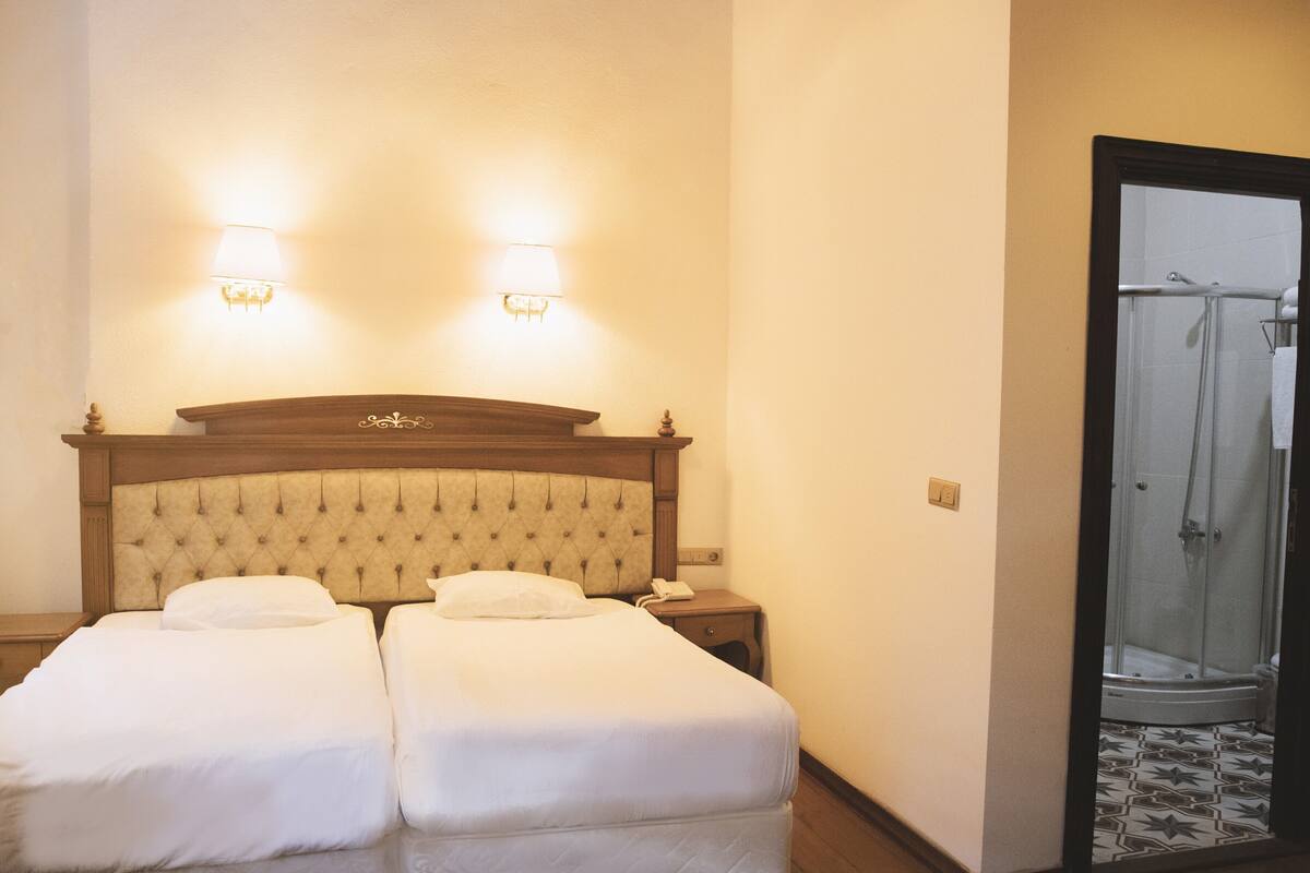 Habitació d'hotel amb llit doble, làmpades de nit, telèfon i zona de dutxa.