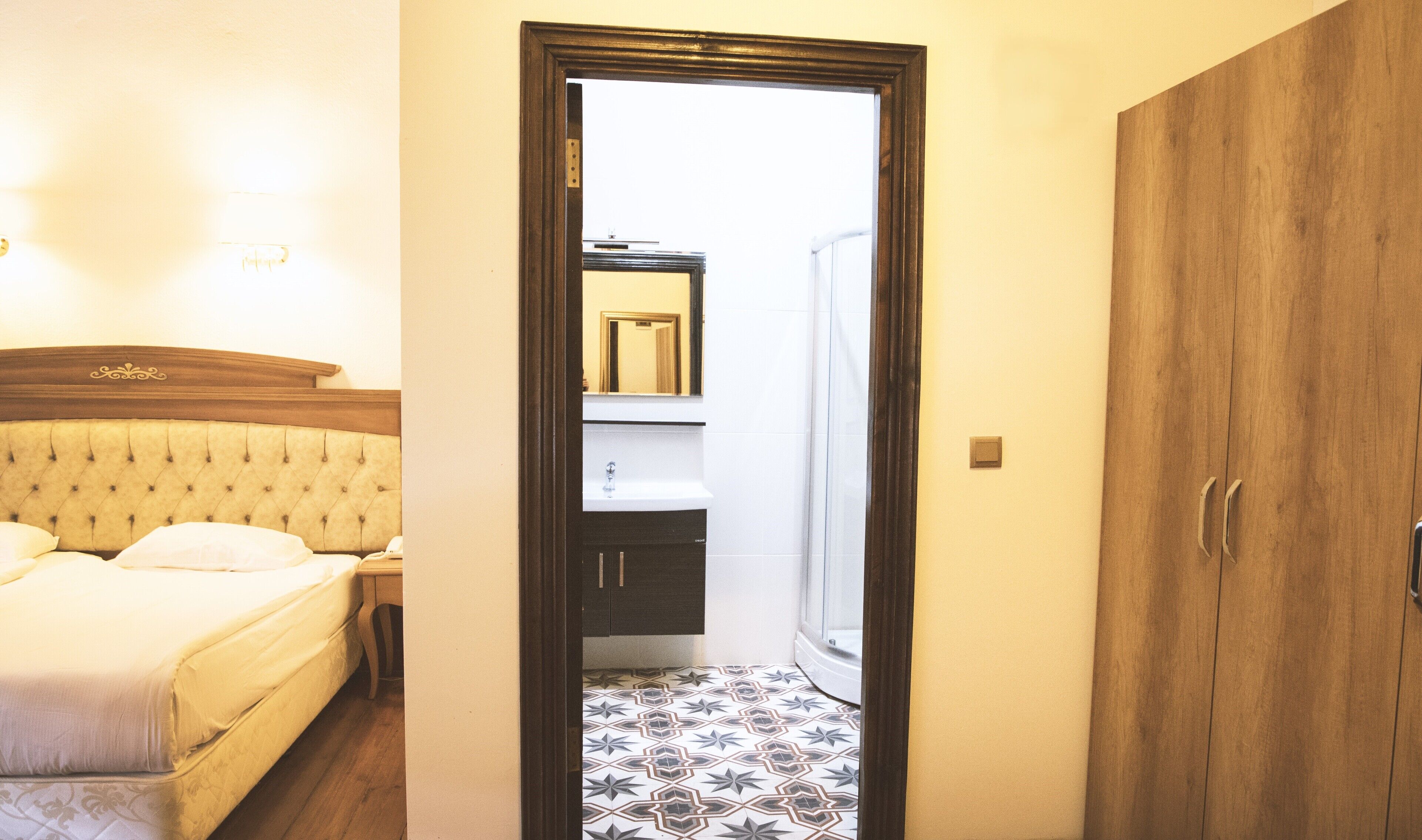 Un dormitorio con una cama, una mesita de noche, un armario de madera y un baño a la vista a través de una puerta abierta.