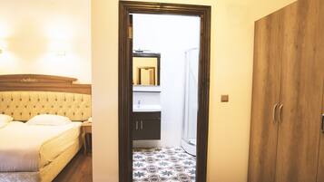 Un dormitorio con una cama, una mesita de noche, un armario de madera y un baño a la vista a través de una puerta abierta.