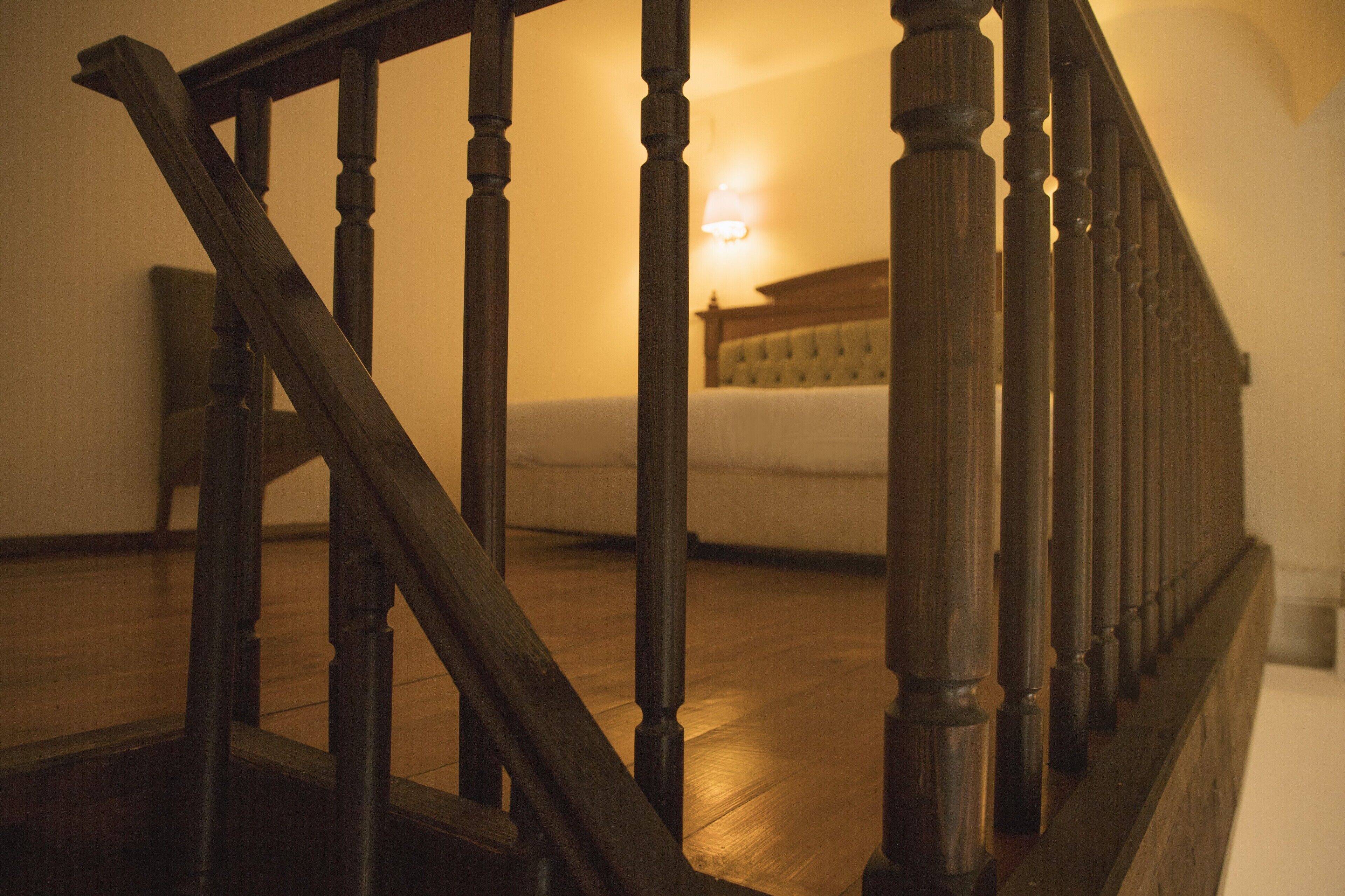A wooden staircase with a handrail leading to a bedroom with a bed and a nightstand.