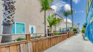 A narrow street lined with wooden fences and palm trees, leading to a building with a beige facade and blue shutters. - Pismo Vacation Multi-Family Home (San Diego)
