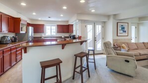 A spacious kitchen with wooden cabinets, a central island, and a dining area with a beige sofa and two barstools. - Pismo Vacation Multi-Family Home (San Diego)