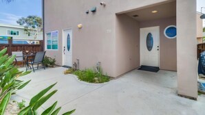 A house with a beige exterior, a front door, and a small porch area with a chair and plants. - Pismo Vacation Multi-Family Home (San Diego)