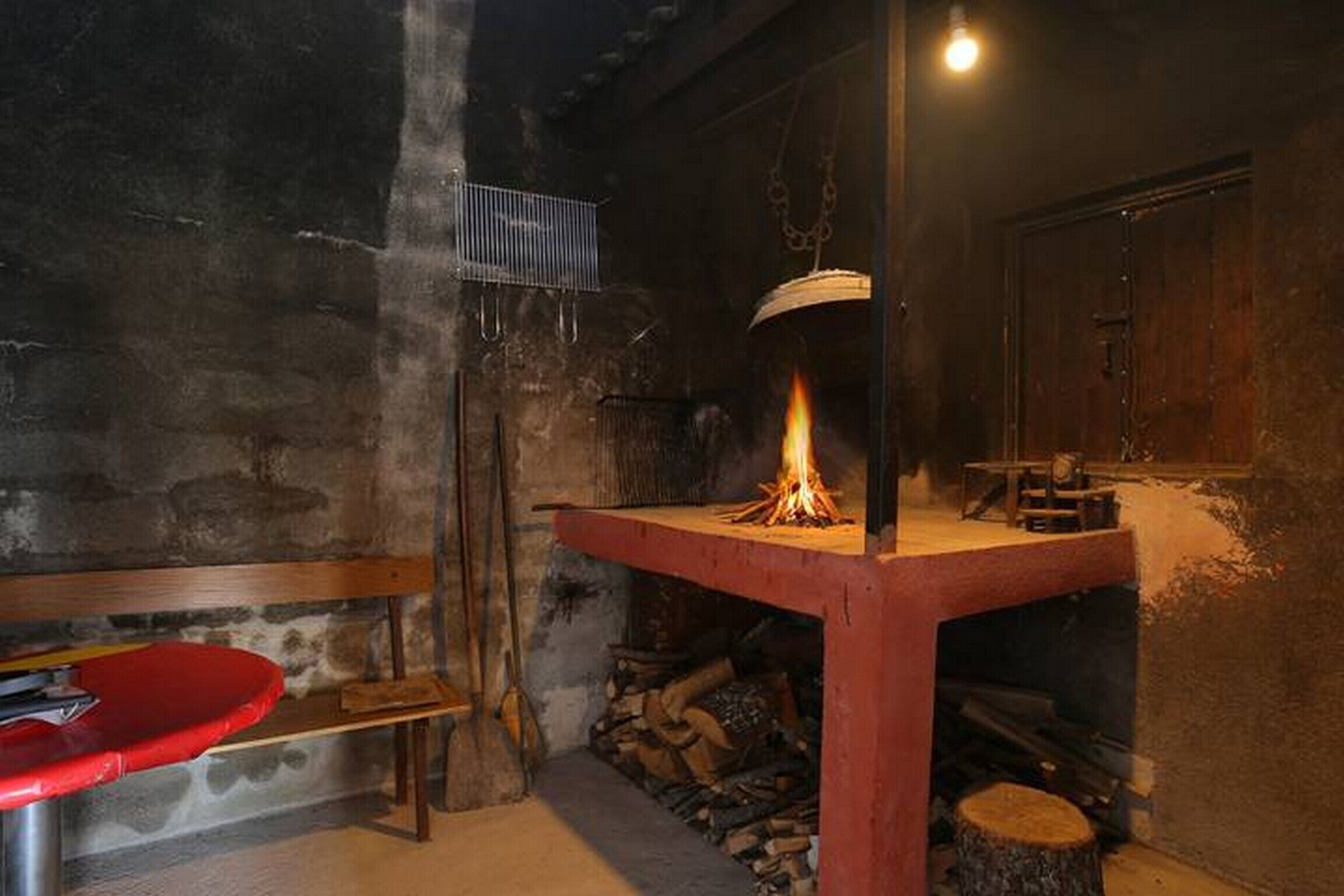 Una habitación rústica con un estufa de leña, un banco y un perchero de metal en la pared.