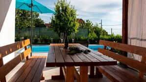 A wooden table with benches, a bottle, and glasses, set outdoors with a pool in the background. - Holiday Home Mons Aureus (Split)