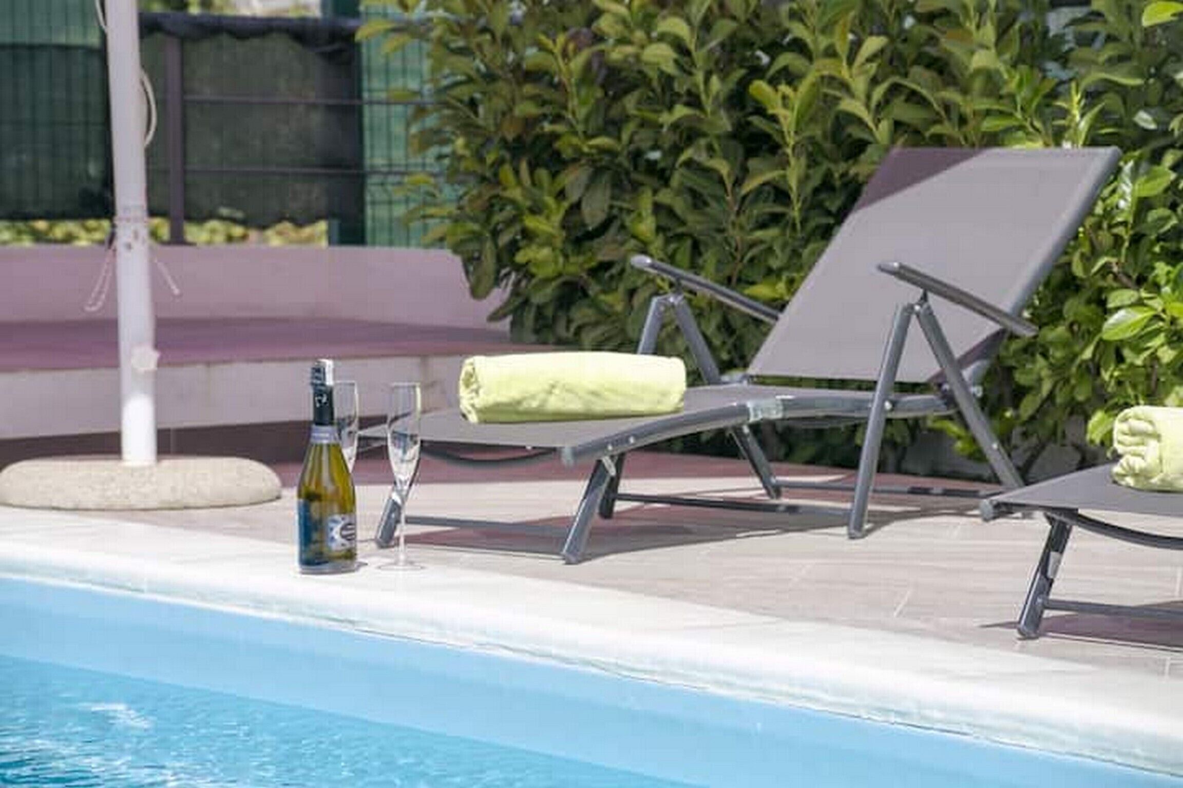 A poolside area with lounge chairs and a bottle of wine.